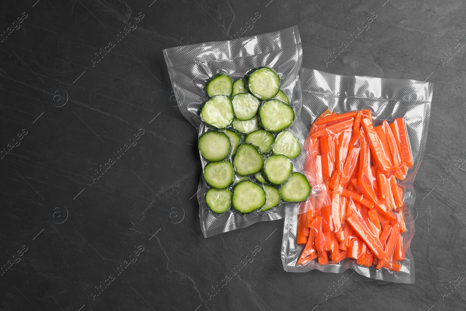 Photo of Sliced vegetables in vacuum packings on dark grey table, flat lay. Space for text