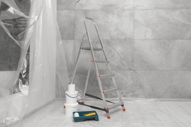 Photo of Metallic folding ladder and painting tools near grey wall indoors