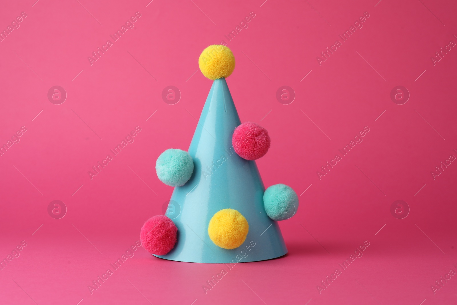 Photo of One light blue party hat with pompoms on pink background