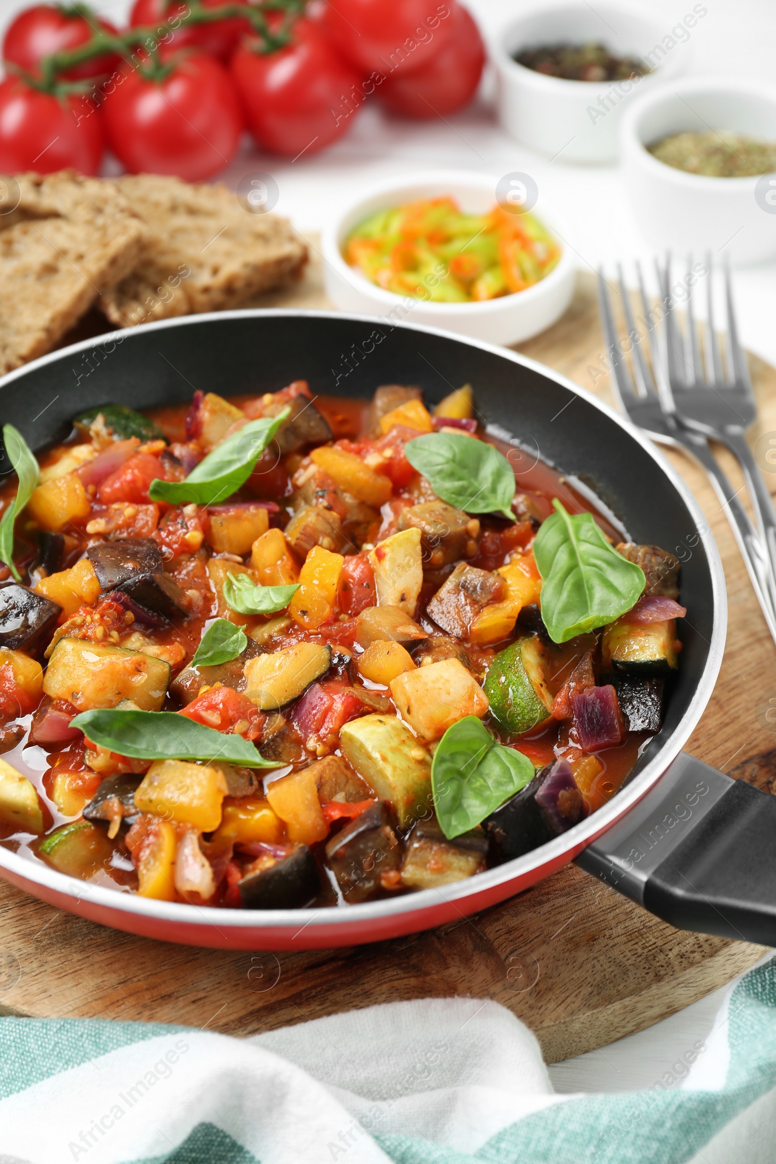 Photo of Frying pan with tasty ratatouille on wooden board, closeup