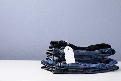 Photo of Stack of stylish jeans with tag on table