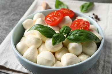 Delicious mozzarella balls, tomatoes and basil leaves in bowl on table, closeup