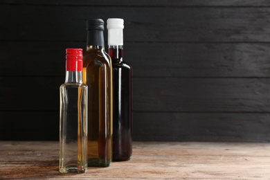 Photo of Bottles with different kinds of vinegar on wooden table. Space for text