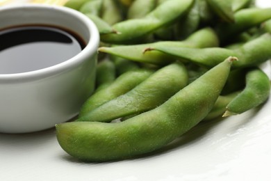 Photo of Green edamame beans in pods served with soy sauce on plate, closeup