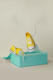 Photo of Box with pair of yellow classic old school sneakers on light grey background