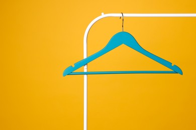 Photo of Blue clothes hanger on metal rack against yellow background