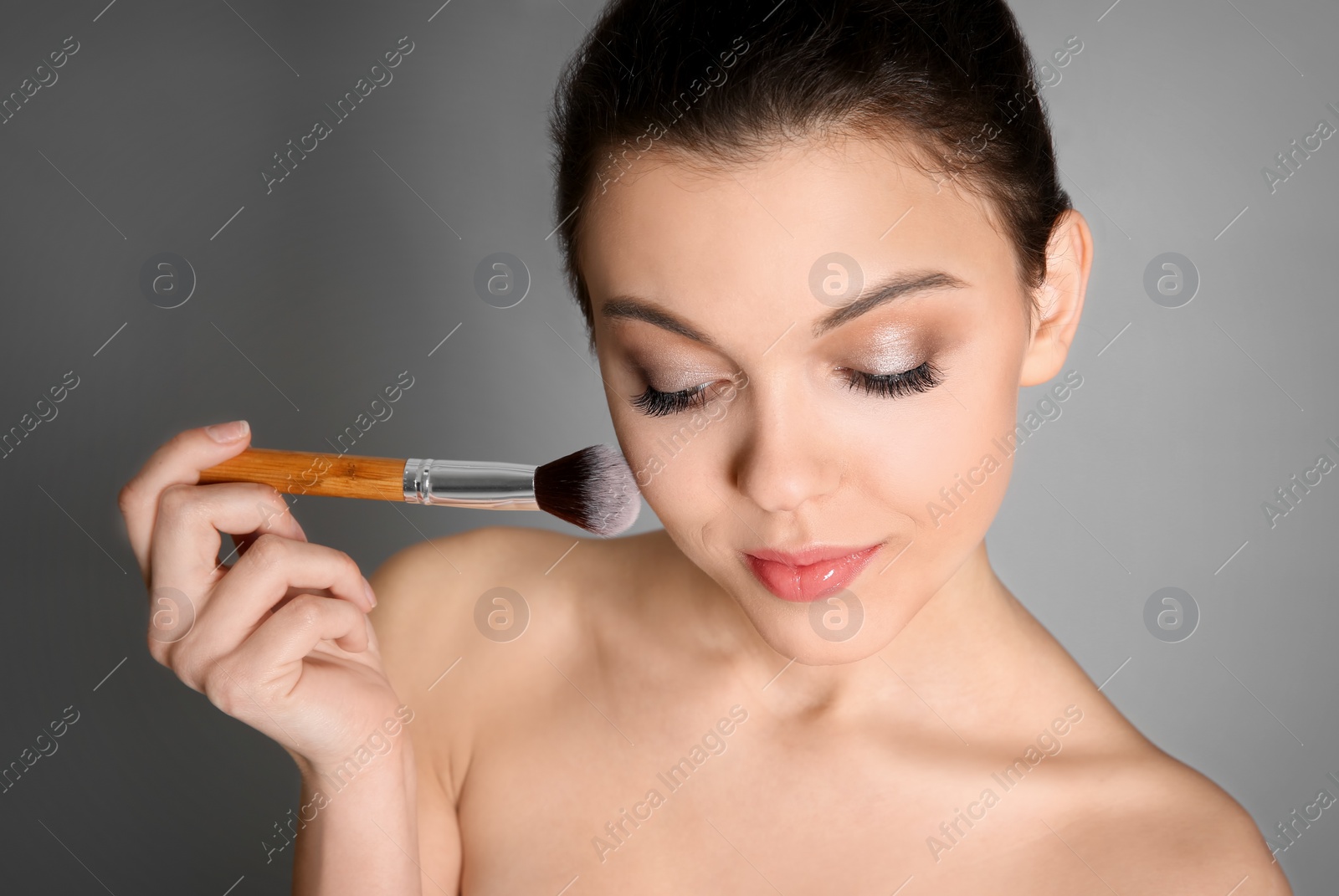 Photo of Young woman applying makeup on grey background. Professional cosmetic products