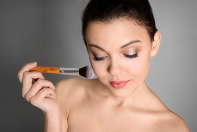 Young woman applying makeup on grey background. Professional cosmetic products