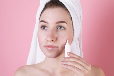 Photo of Young woman with acne problem applying cosmetic product onto her skin on pink background