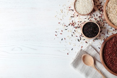 Photo of Flat lay composition with brown and other types of rice on white wooden background. Space for text