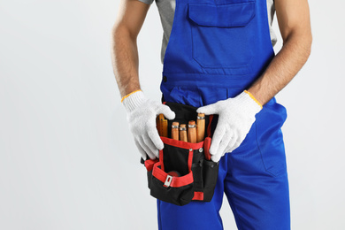 Carpenter with tool belt on light background, closeup