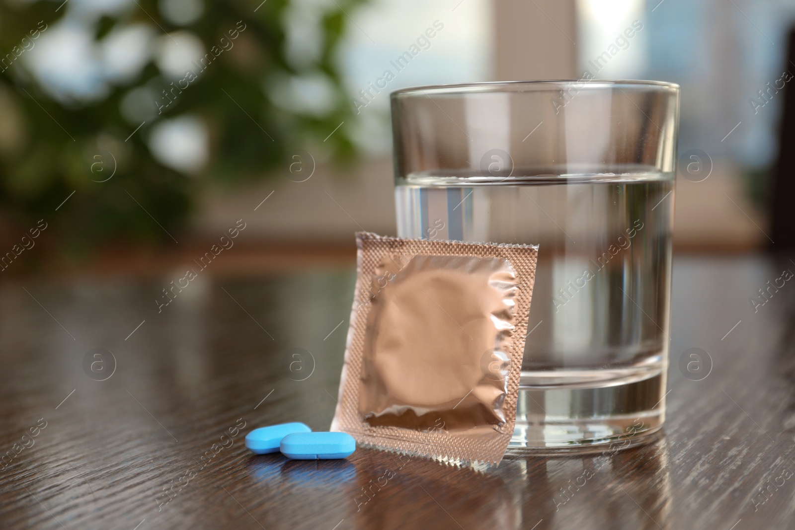 Photo of Glass of water, condom and pills on wooden table indoors, closeup with space for text. Potency problem concept