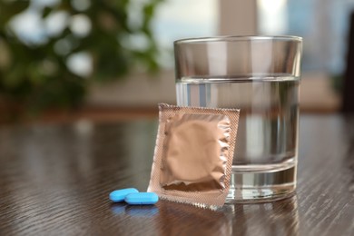 Photo of Glass of water, condom and pills on wooden table indoors, closeup with space for text. Potency problem concept