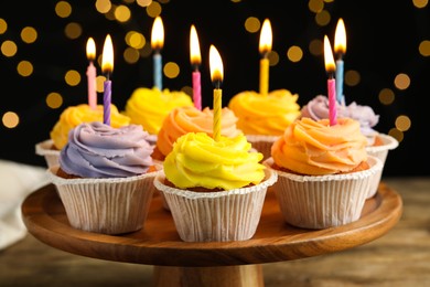 Tasty birthday cupcakes on wooden stand against blurred lights, closeup