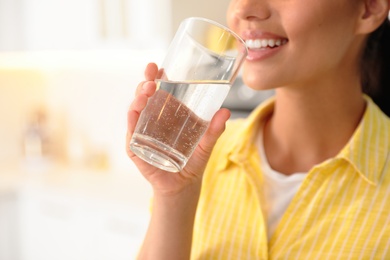 Photo of Young woman drinking pure water from glass in kitchen, closeup