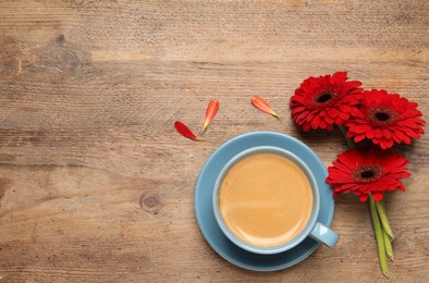 Cup of coffee and red gerbera flowers on wooden table, flat lay. Space for text