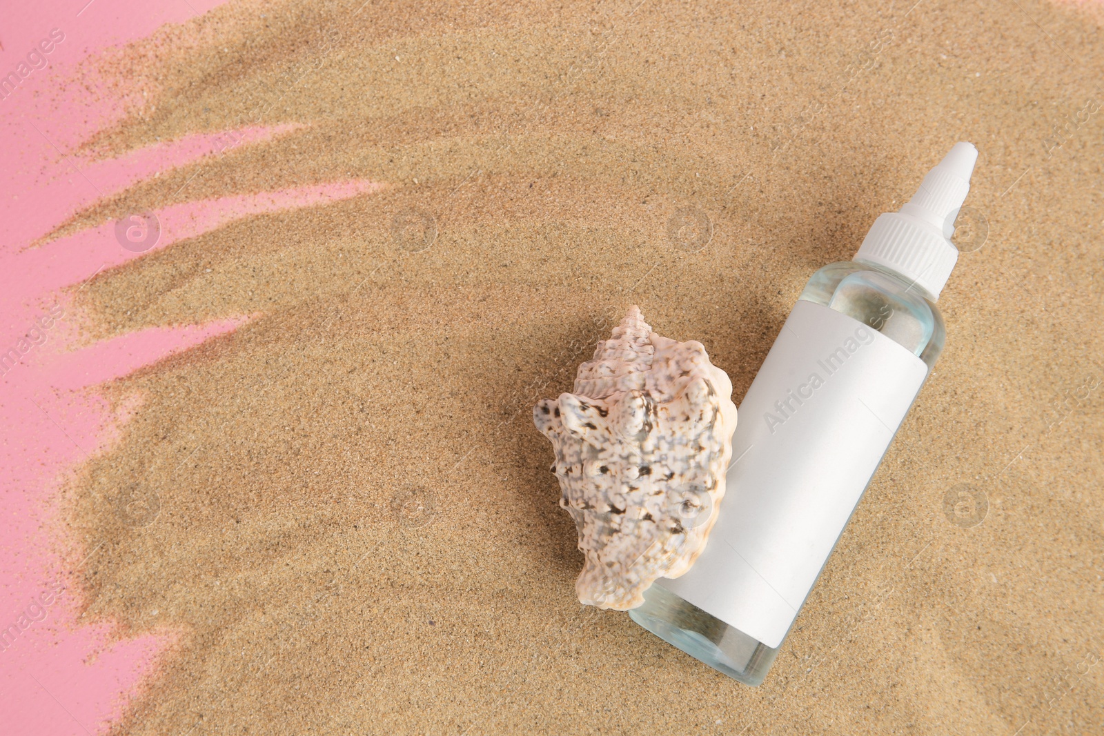 Photo of Bottle of serum and seashell on sand against pink background, top view. Space for text