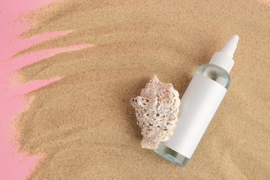 Bottle of serum and seashell on sand against pink background, top view. Space for text