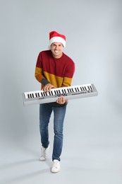 Photo of Man in Santa hat playing synthesizer on light grey background. Christmas music