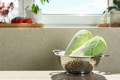 Fresh Chinese cabbages in colander on light wooden table indoors. Space for text