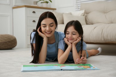 Photo of Young mother and her daughter reading book at home