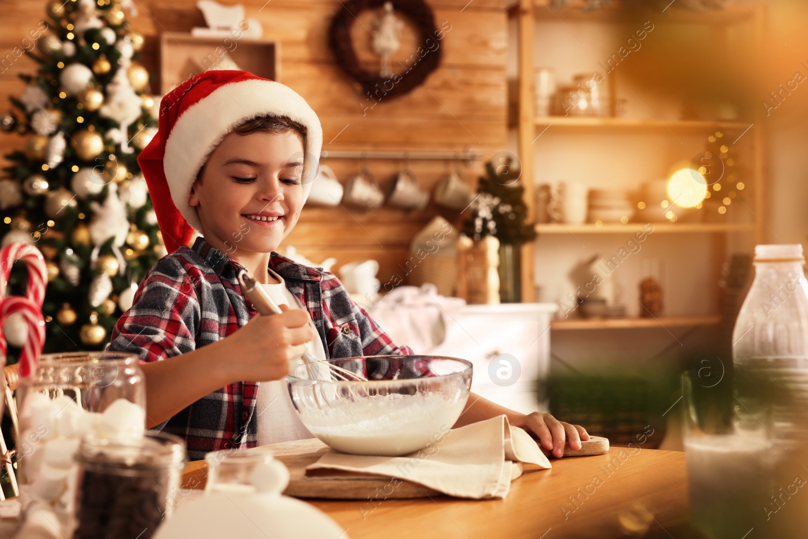 Photo of Cute little boy in Santa hat making dough for Christmas cookies at home