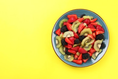 Plate of yummy fruit salad on yellow background, top view. Space for text