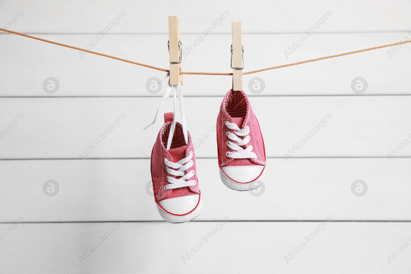 Photo of Cute pink baby sneakers drying on washing line against white wall