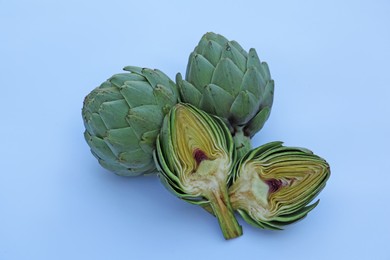 Photo of Cut and whole fresh raw artichokes on light blue background