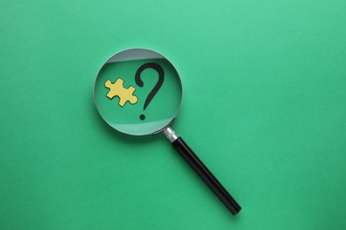 Photo of Magnifying glass over paper puzzle and question mark on green background, top view