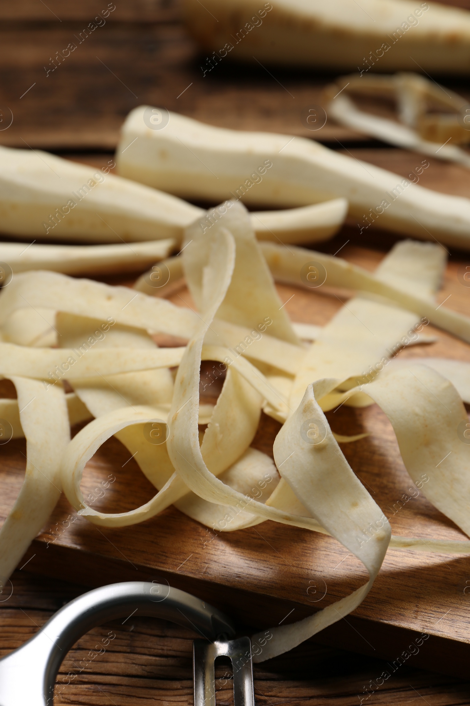 Photo of Peeled fresh parsnips and strips on wooden table, closeup