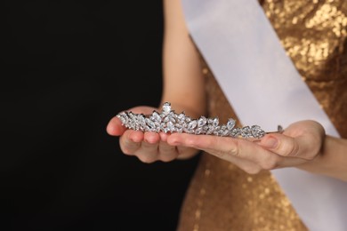 Woman in dress holding tiara on black background, closeup. Space for text