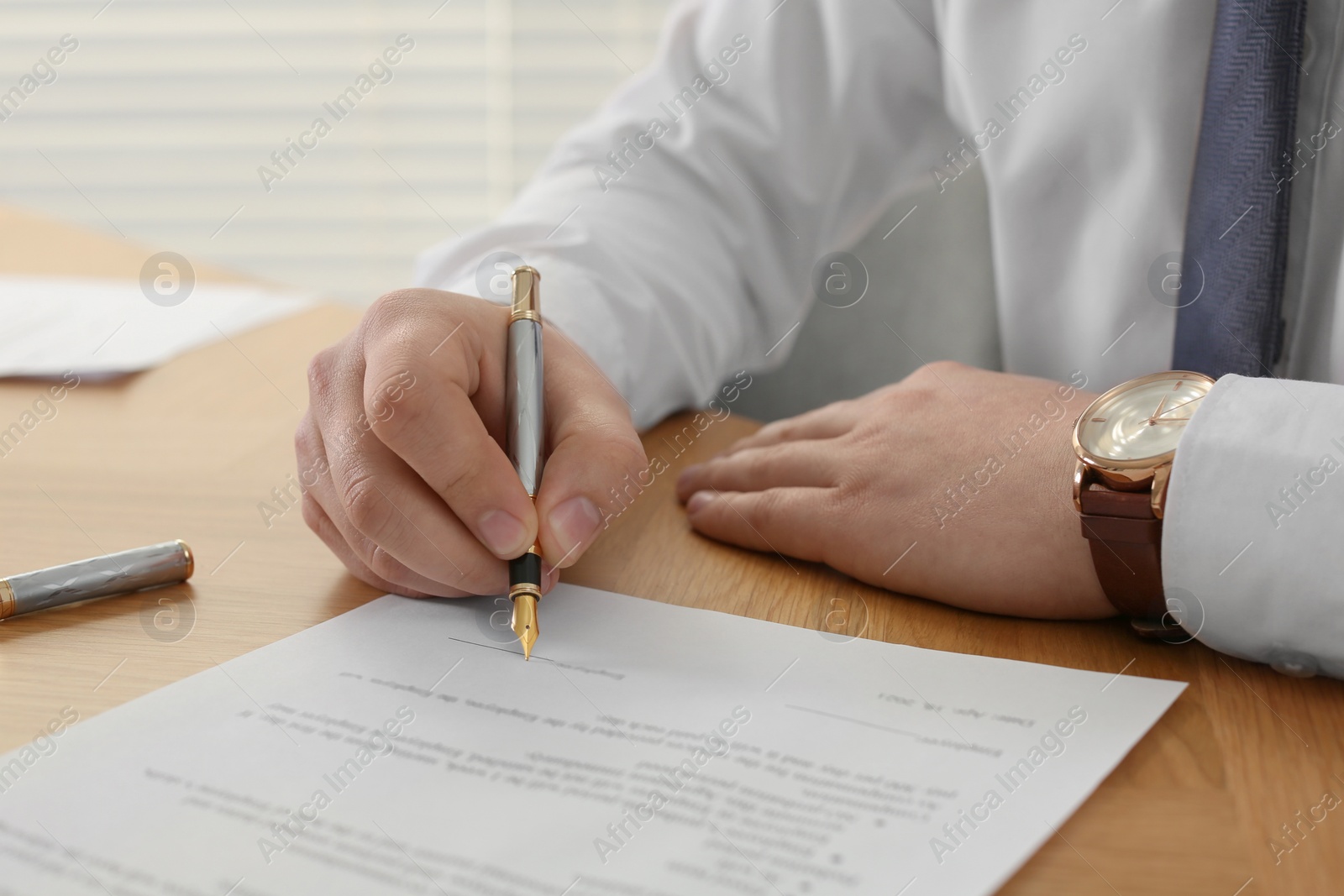 Photo of Notary signing document at wooden table indoors, closeup