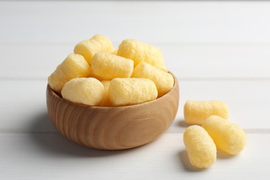 Photo of Bowl of delicious crispy corn sticks on white wooden table