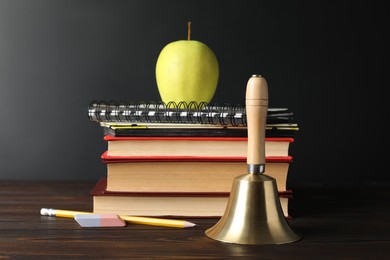 Golden bell, apple and school stationery on wooden table near blackboard