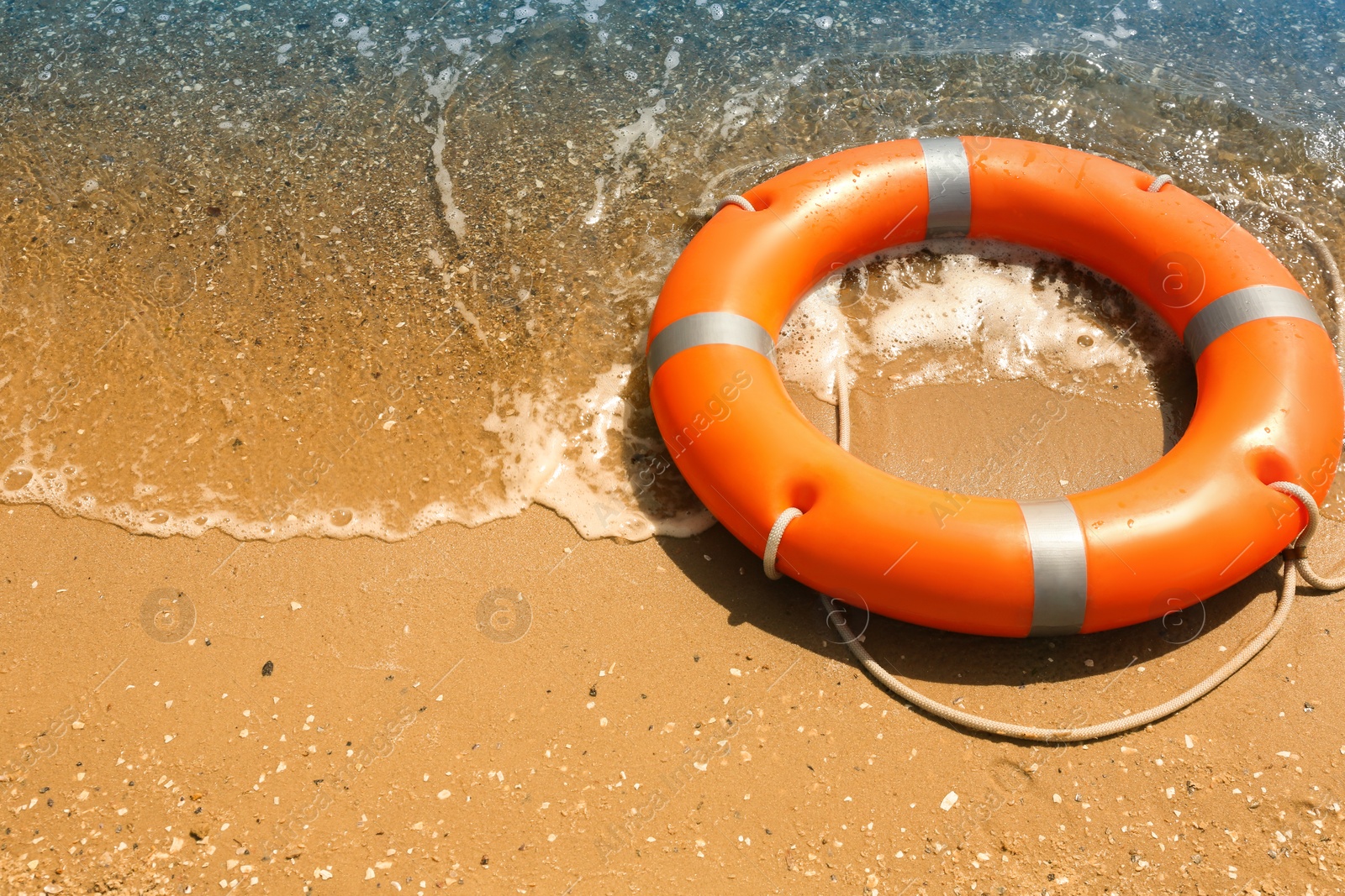 Photo of Orange life buoy on sand near sea. Emergency rescue equipment