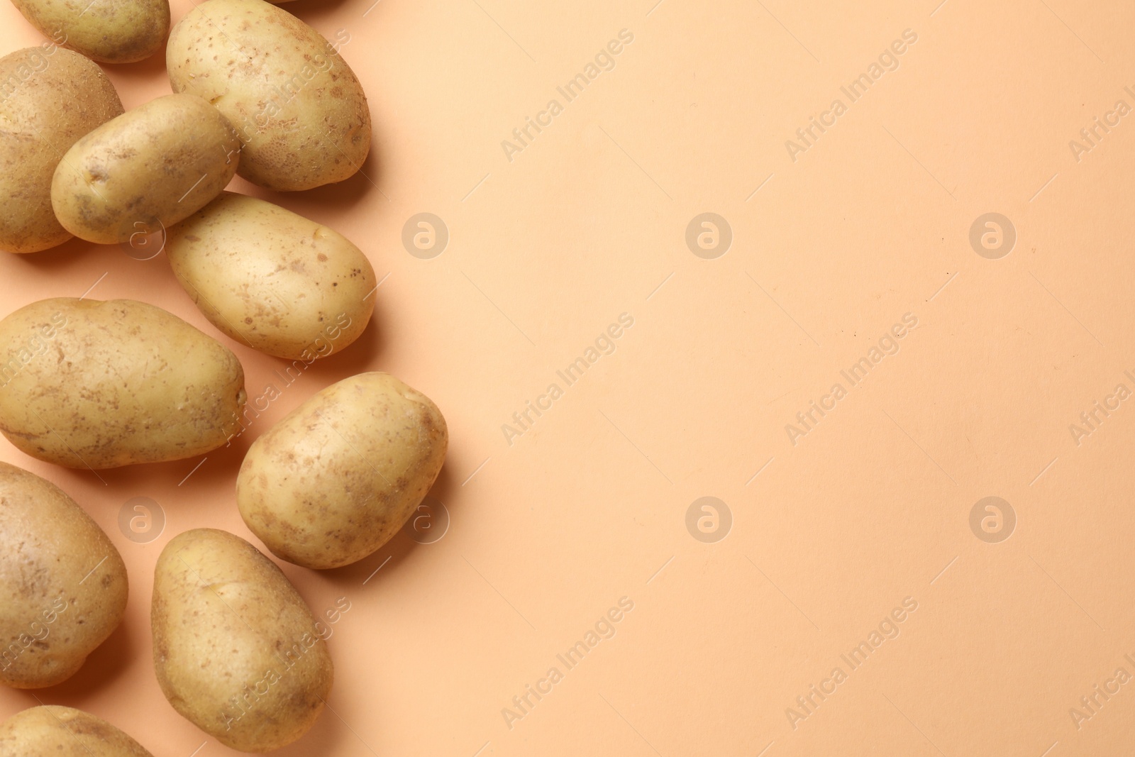 Photo of Fresh raw potatoes on pale orange background, flat lay. Space for text