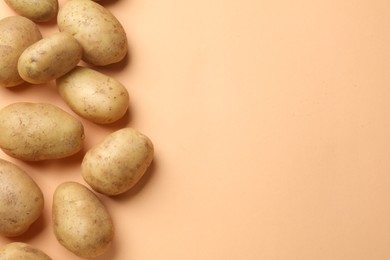 Fresh raw potatoes on pale orange background, flat lay. Space for text