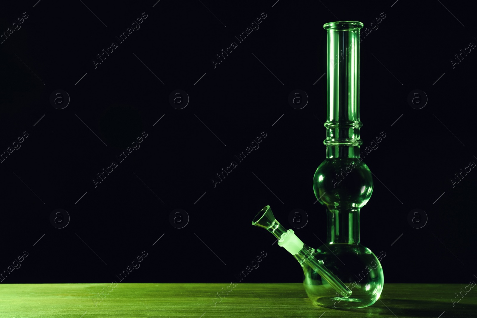 Photo of Glass bong on wooden table against black background, space for text. Smoking device