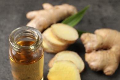 Photo of Glass bottle of ginger essential oil on grey table, closeup. Space for text