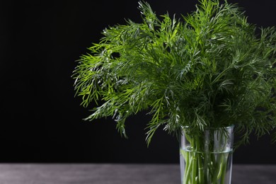 Photo of Fresh dill in glass on grey table against black background, closeup. Space for text