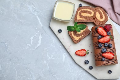 Photo of Tasty chocolate cake roll with cream and berries on light grey marble table, flat lay. Space for text