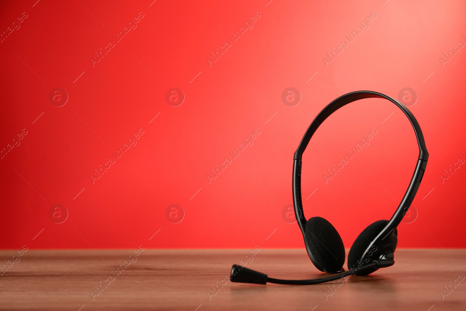 Photo of Headset on wooden table against red background, space for text