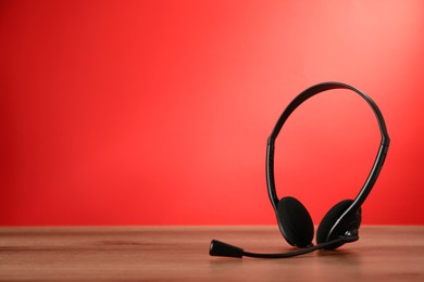 Photo of Headset on wooden table against red background, space for text