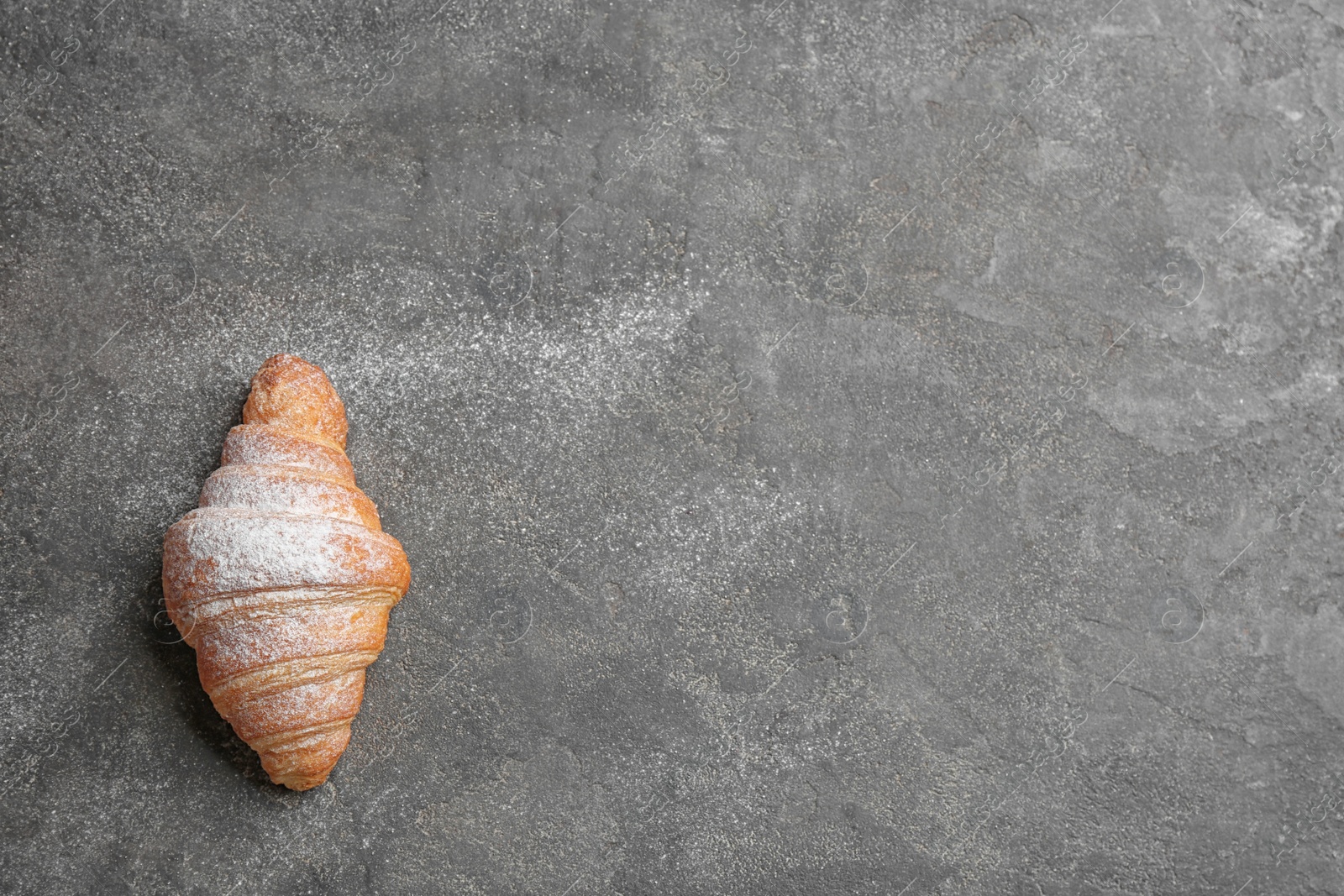 Photo of Tasty croissant with powdered sugar and space for text on grey background, top view. French pastry