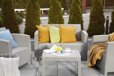 Beautiful rattan garden furniture, soft pillows and different decor elements in backyard