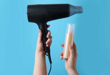 Photo of Woman holding spray bottle with thermal protection and hairdryer on light blue background, closeup