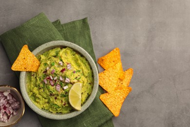 Photo of Bowl of delicious guacamole, nachos chips and lime on grey table, flat lay. Space for text