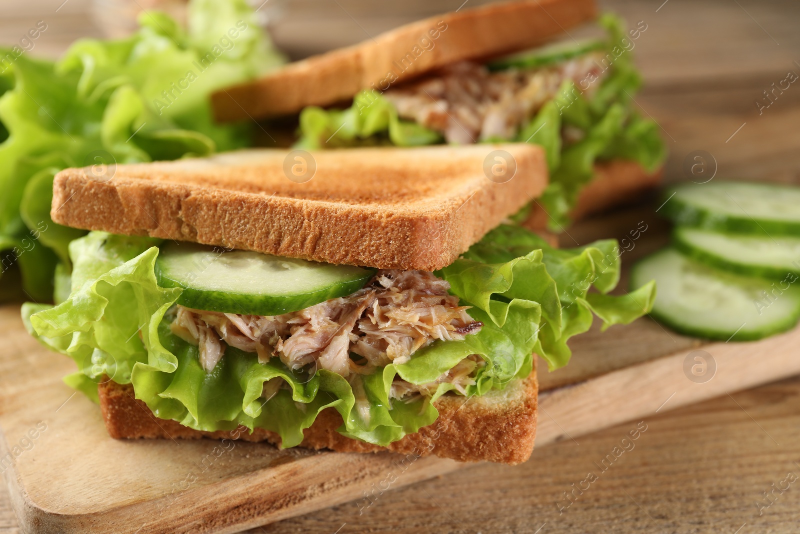 Photo of Delicious sandwiches with tuna, cucumber and lettuce leaves on wooden table, closeup