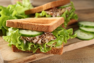 Delicious sandwiches with tuna, cucumber and lettuce leaves on wooden table, closeup